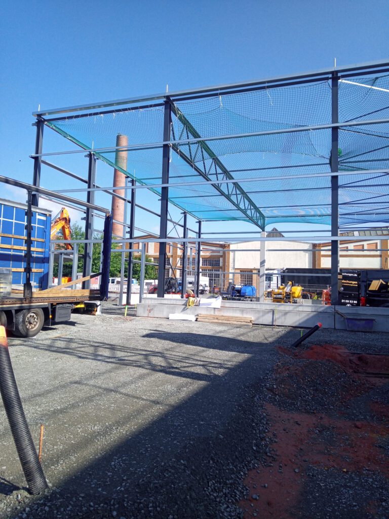 Bauvorhaben Stahlgruber Kaiserslautern: Stahlkonstruktion mit Sicherheitsnetz und Baumaschinen auf der Baustelle